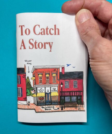 A hand holding a small illustrated journal against a bright teal background. The cover features a colorful streetscape of downtown Jonesborough with the title “To Catch A Story” in bold serif letters. Landmarks like the Lollipop Shop, Candy Toy Store, Whisper Alley, and The Listening Bench are labeled with handwritten arrows.